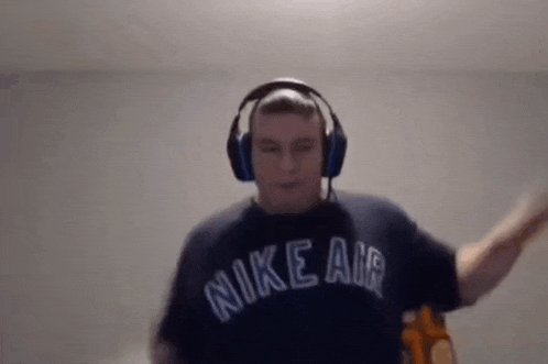 a man wearing headphones and a nike air shirt is dancing in front of a camera .
