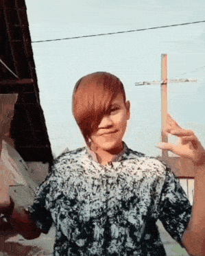 a young boy with red hair and a black and white shirt is giving a peace sign .