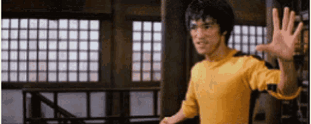 a man in a yellow shirt is waving his hand while standing in front of a window .