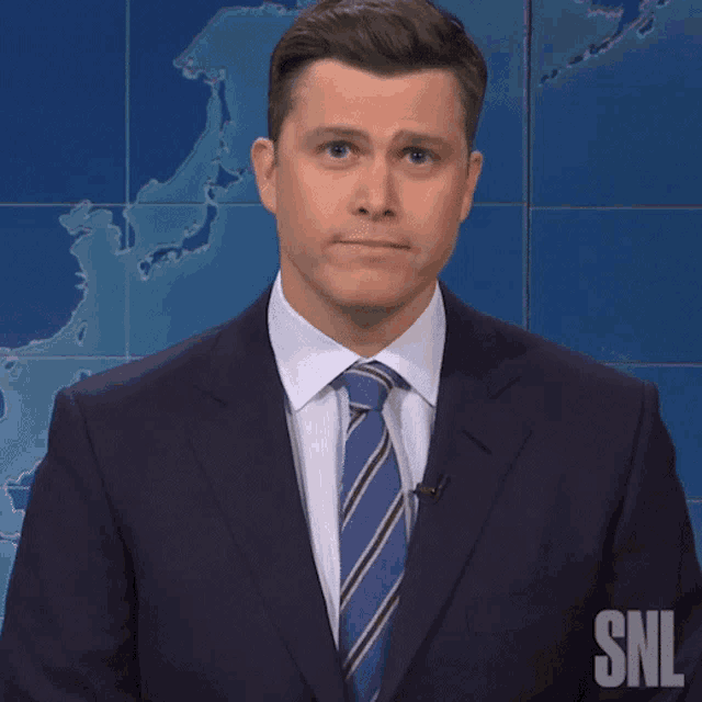 a man in a suit and tie is standing in front of a snl banner