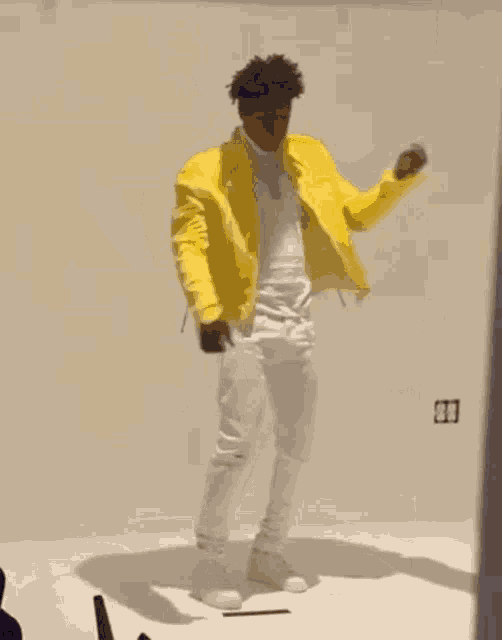 a man in a yellow jacket and white pants is dancing on a white floor .