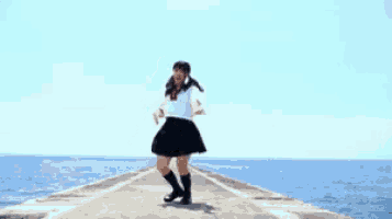 a girl in a school uniform is running on a pier near the ocean