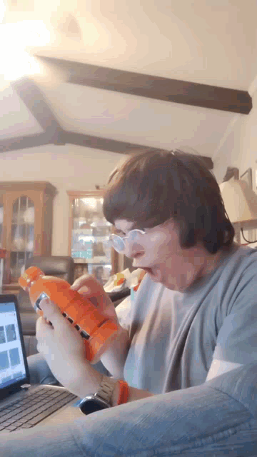 a man wearing glasses is holding an orange nerf gun in front of a laptop