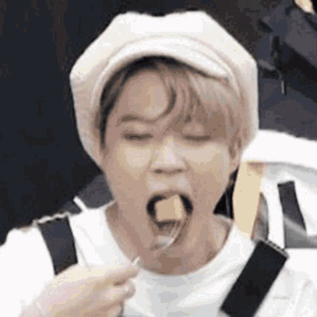 a man wearing a hat is eating a piece of food with a fork .