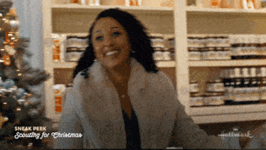 a woman in a fur coat is smiling in front of a shelf with bottles on it that says hallmark