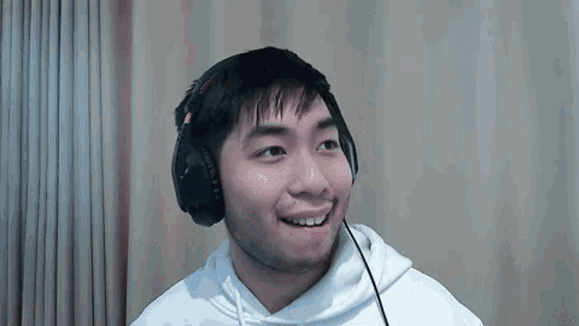 a man wearing headphones and a white hoodie is smiling and looking at the camera .