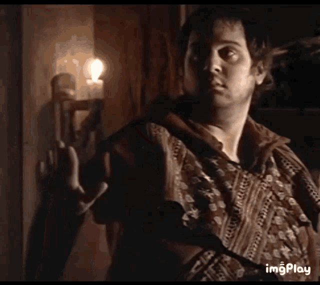 a man is standing in front of a candle in a dark room