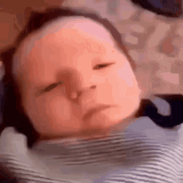 a baby is laying on a bed with his eyes closed and a striped shirt on .