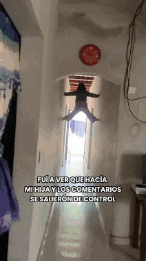 a girl is flying through the air in a hallway with a red clock on the wall