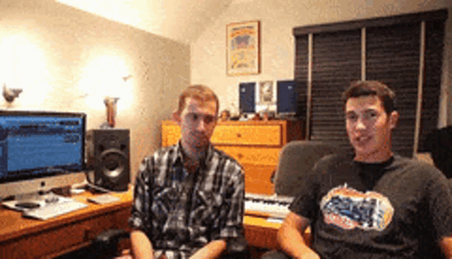 two men are sitting in a room with a keyboard and a computer monitor