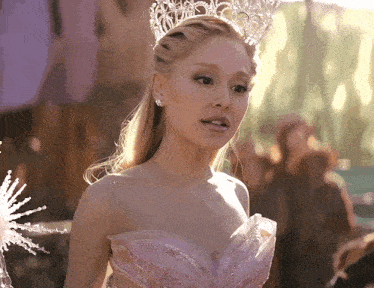 a woman wearing a crown and a pink dress looks at the camera