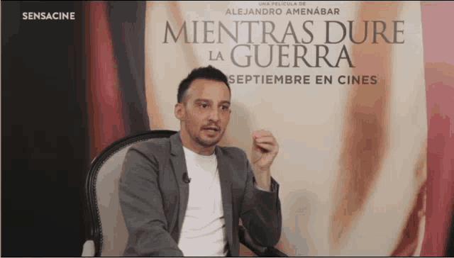 a man is sitting in front of a sign that says " mientras dure la guerra "