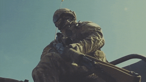 a soldier is holding a sniper rifle against a clear blue sky