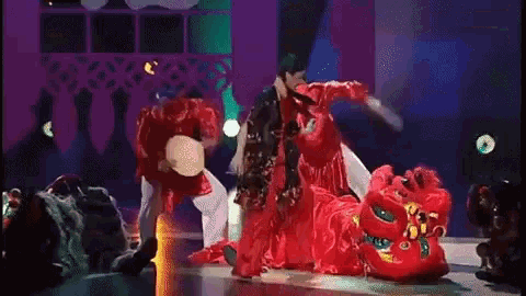 a group of people are dancing on a stage with a red dragon in the middle .