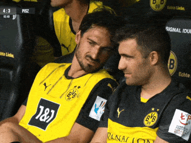 two soccer players wearing yellow and black jerseys with bvb on them sit in a locker room
