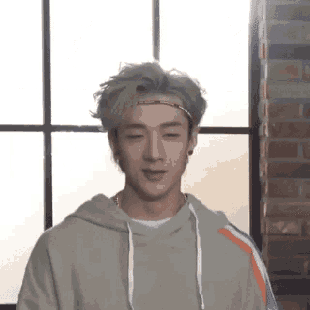 a young man wearing a headband and a hoodie is standing in front of a window in a room .