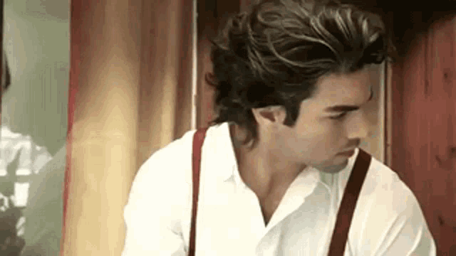 a man in a white shirt and red suspenders is standing in a room .