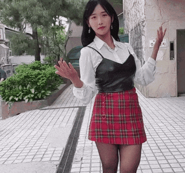 a woman wearing a plaid skirt and tights is standing in front of a building