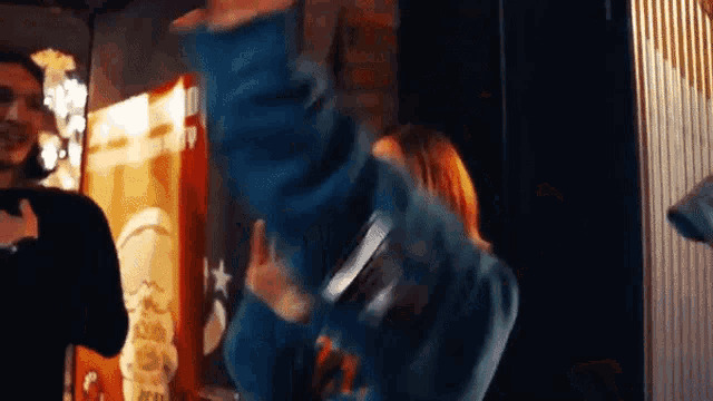 a woman in a blue jacket is dancing in front of a sign that says ' army ' on it