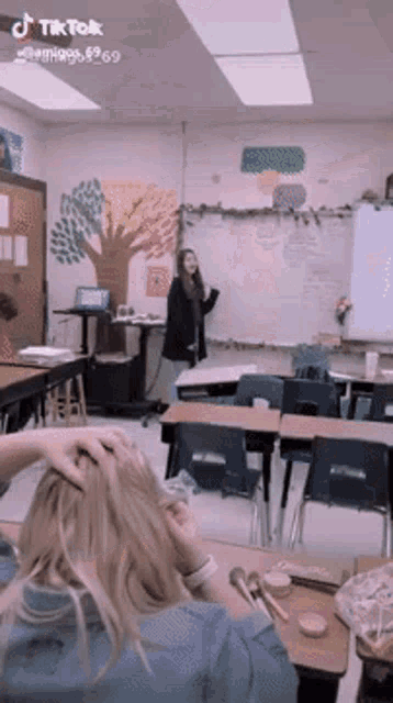a woman is standing in front of a whiteboard in a classroom with a tree on the wall behind her ..