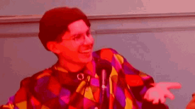 a man wearing glasses and a colorful shirt is standing in front of a microphone .