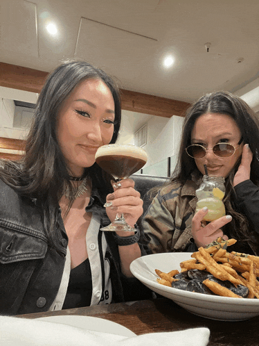 two women are sitting at a table with a plate of food and a martini