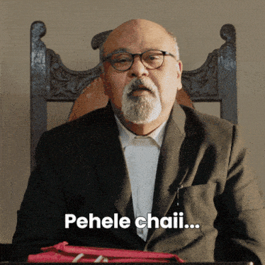 a man with a beard and glasses is sitting in a chair and says pehele chaii