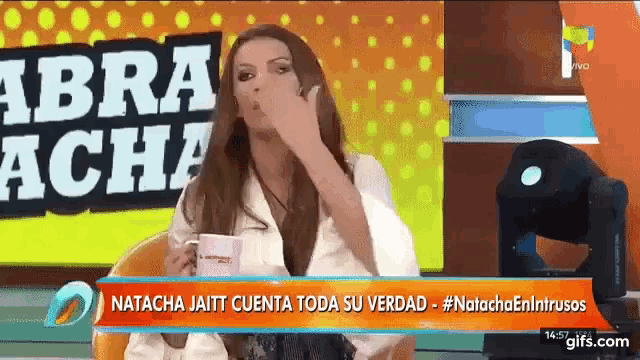 a woman covering her mouth while sitting in front of a sign that says " abra acha "