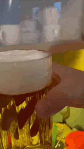 a close up of a person holding a glass of beer with foam on top