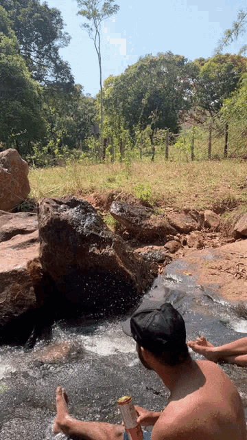 a man in a black hat sits in a stream with his feet in the water
