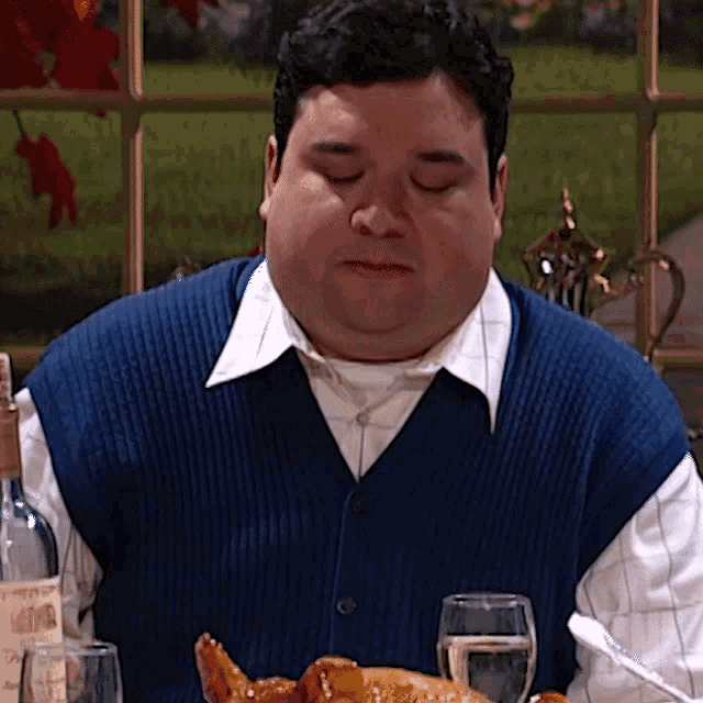 a man in a blue vest sits at a table with a bottle of wine and a glass of water