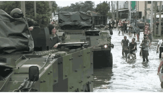 a group of people are walking through a flooded street with military vehicles in the foreground
