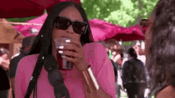 a woman in a pink shirt and sunglasses is drinking from a cup .