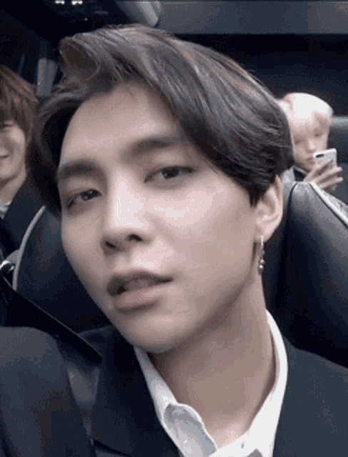 a close up of a young man wearing a suit and earrings sitting in a car .
