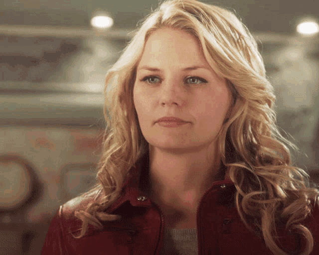 a blonde woman wearing a red jacket is looking at the camera