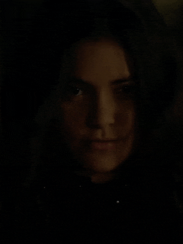 a woman is smiling in the dark and looking at the camera .