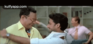 a man in a yellow shirt is hugging another man in a room .