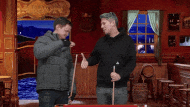 two men holding pool cues in a room with a sign that says lion