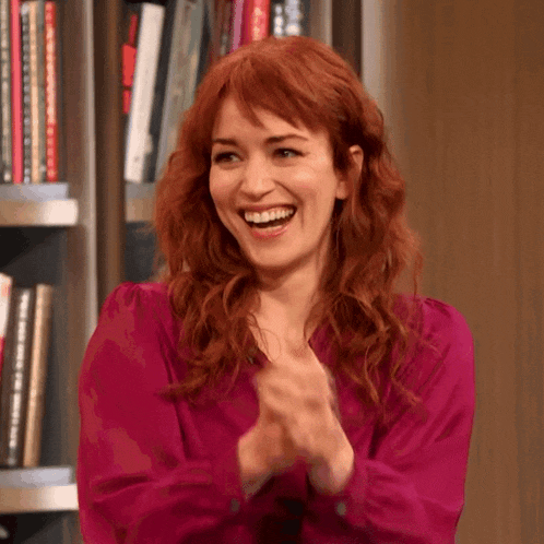 a woman with red hair is clapping her hands and smiling