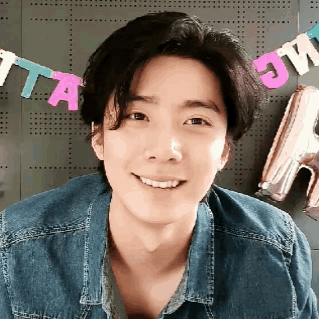 a young man wearing a denim shirt is smiling in front of a banner that says " ta "