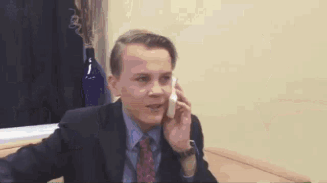 a young man in a suit is talking on a cell phone .
