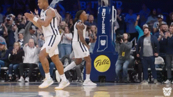 two basketball players are celebrating on the court in front of a butler advertisement