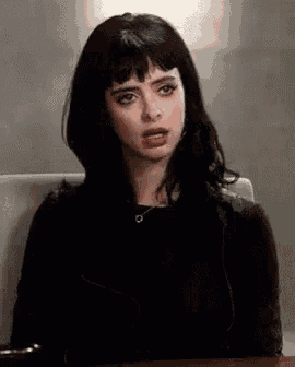 a woman with black hair and bangs is sitting at a table with her mouth open .