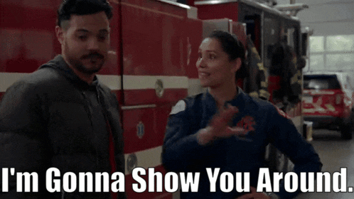 a man and a woman standing in front of a fire truck with the words i 'm gonna show you around written below them
