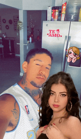 a man and a woman pose in front of a refrigerator with a sticker that says te amo