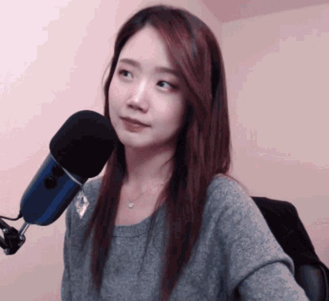 a woman in a grey sweater stands in front of a microphone