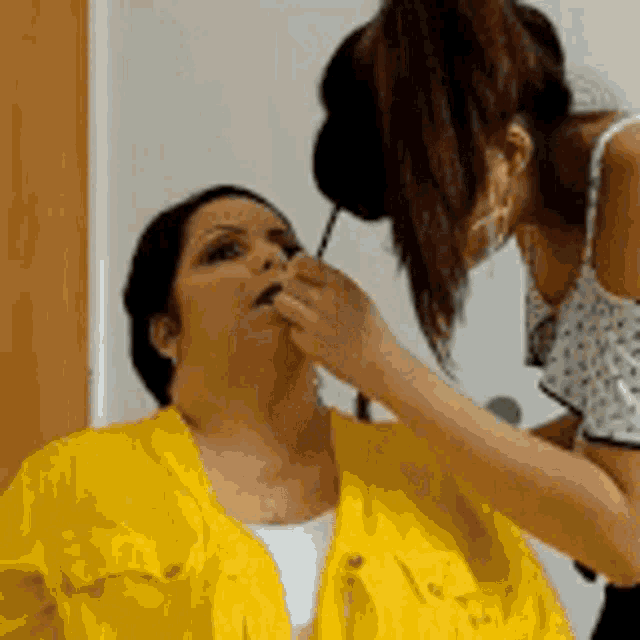 a woman in a yellow jacket is getting her makeup done