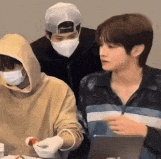 a group of young men wearing masks are sitting around a table .