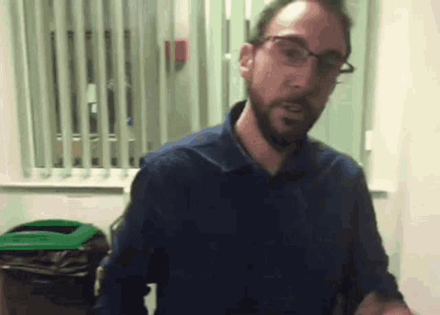 a man with glasses and a beard standing in front of a window