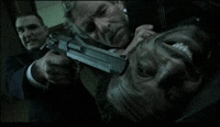 a man in a suit is holding a gun to another man 's face